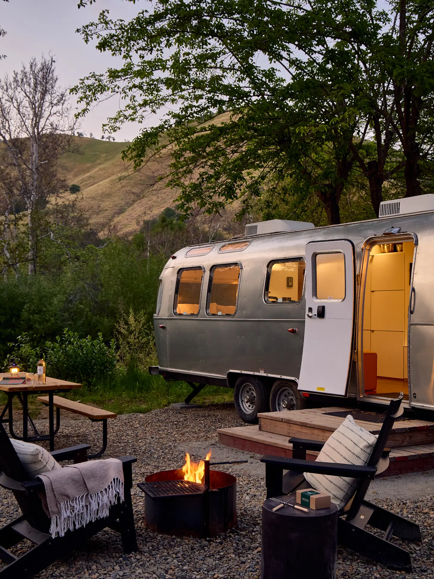 An illuminated Airstream and fire pit at the offsite grounds at dusk